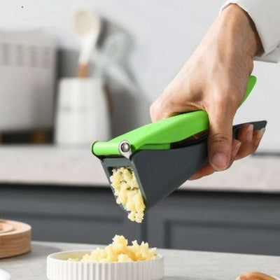 Manual garlic press gadget in use, effortlessly mashing garlic over a dish on a kitchen counter.